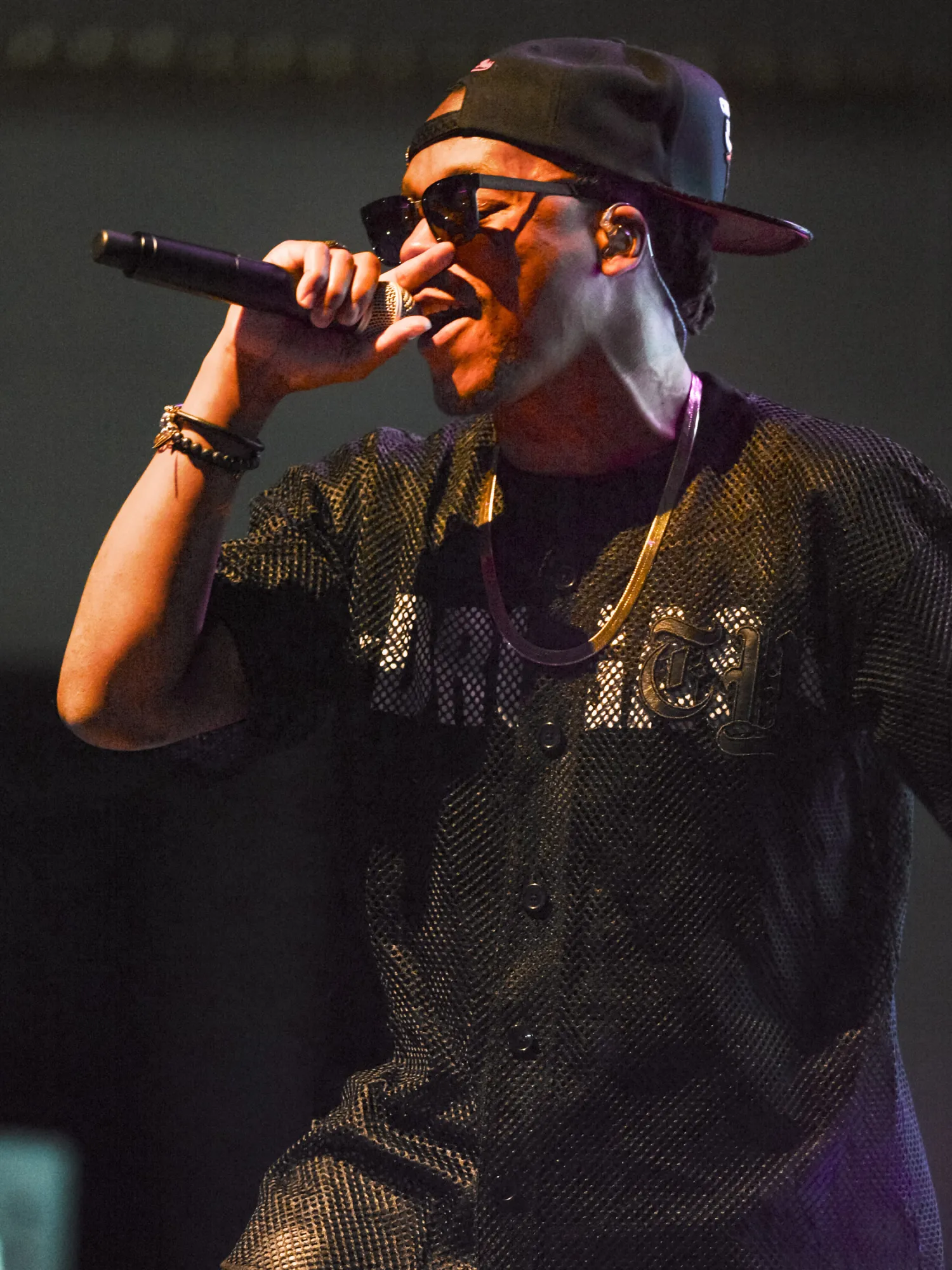 Lupe Fiasco holds a microphone close to his mouth.